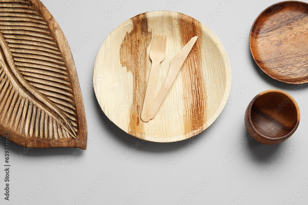 Wooden plates, board and cutlery on light background