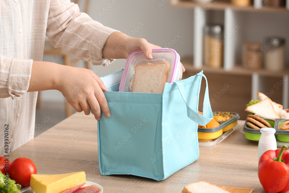 Mother packing meal for school lunch on table in kitchen