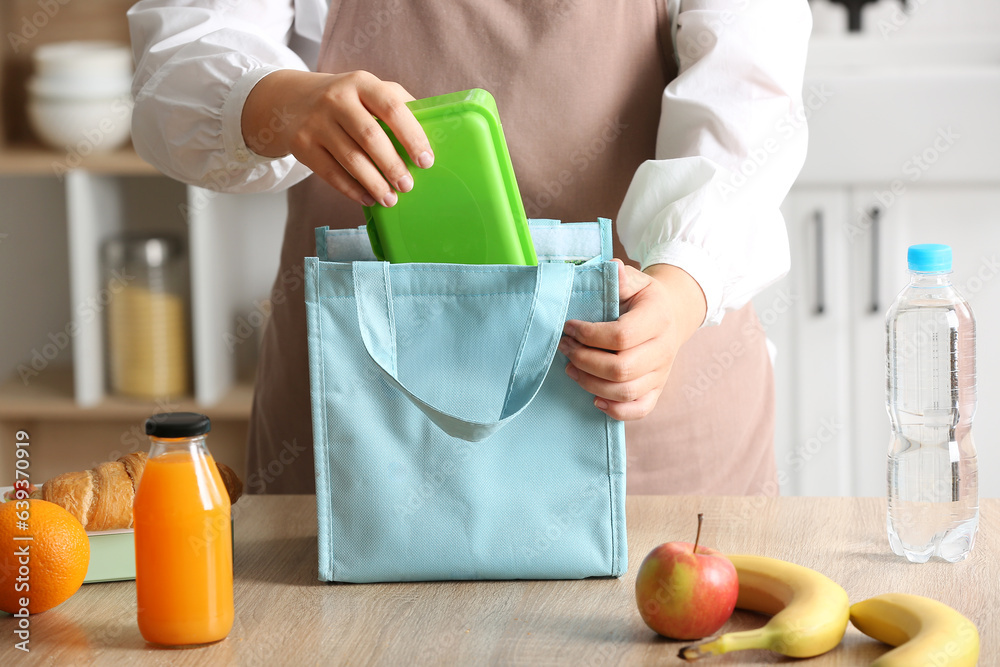 Mother packing meal for school lunch on table in kitchen