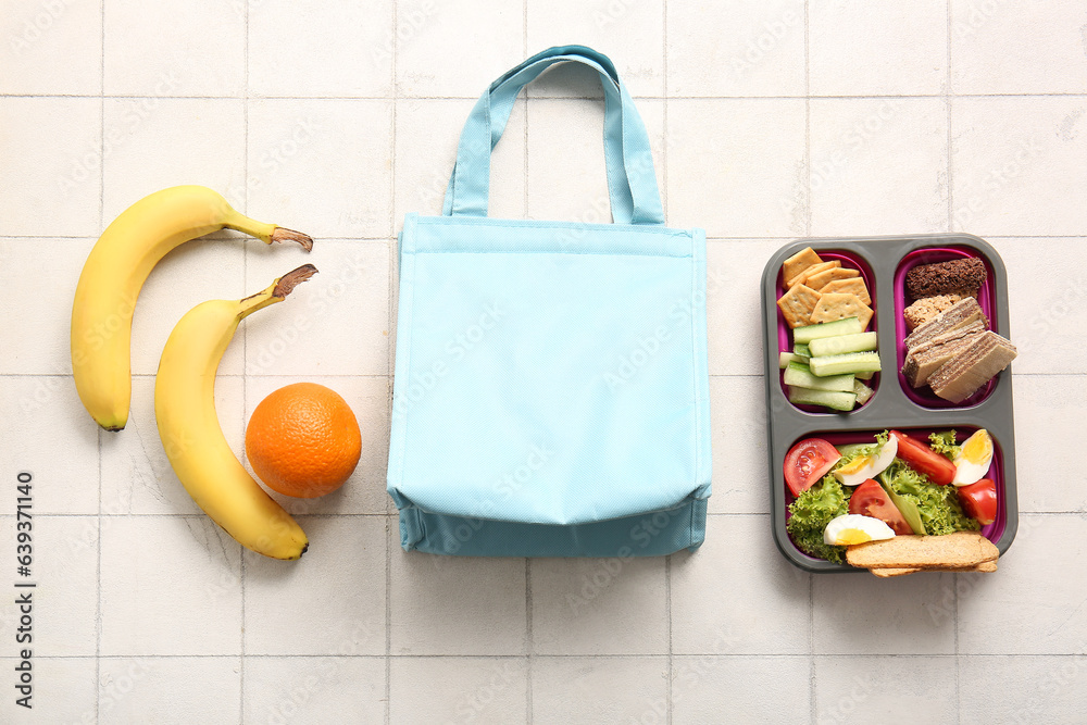 Bag, lunchbox with delicious food and fruits on white tile background