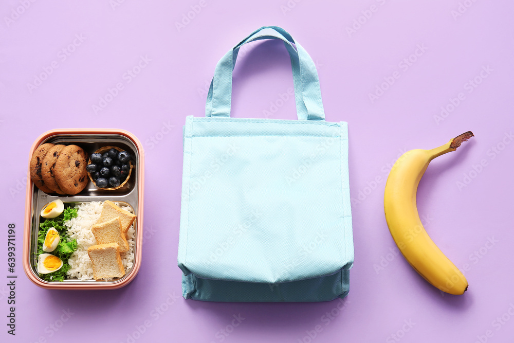 Bag, lunchbox with delicious food and banana on lilac background