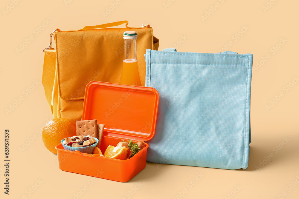 Bags, lunchbox with delicious food and bottle of juice on yellow background