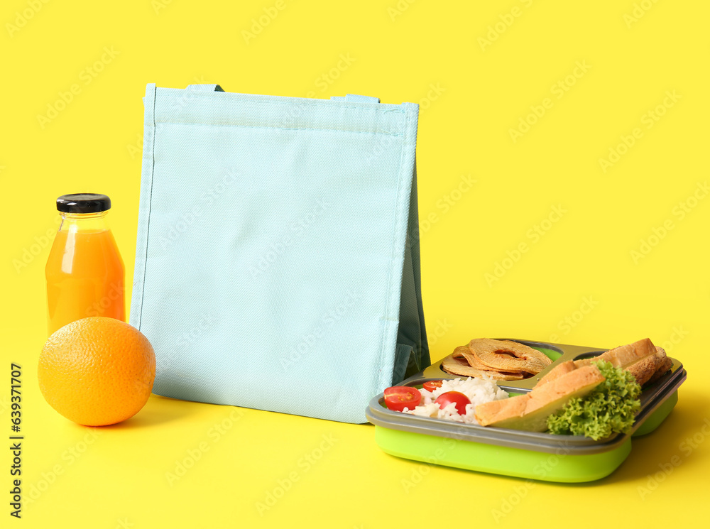 Bag, lunchbox with delicious food and bottle of juice on yellow background