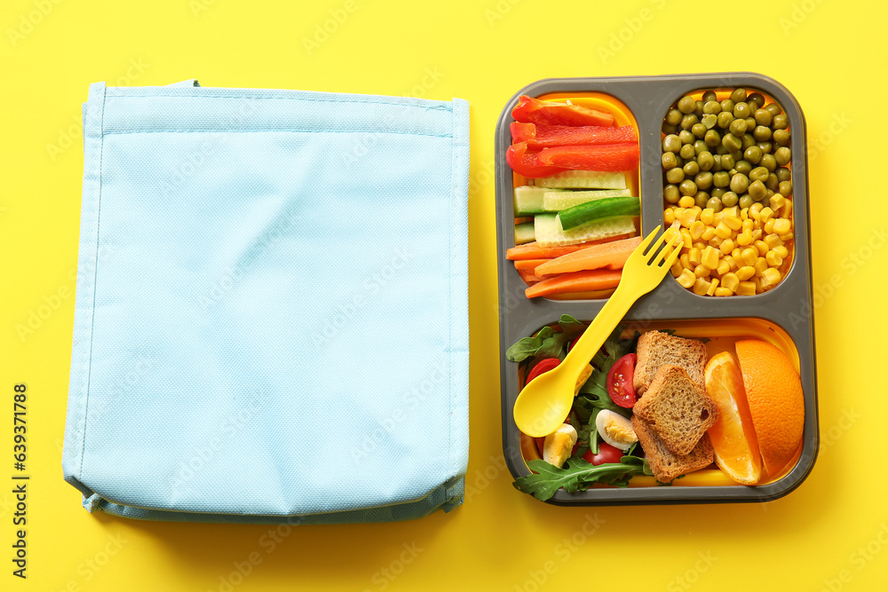 Bag and lunchbox with delicious food on yellow background