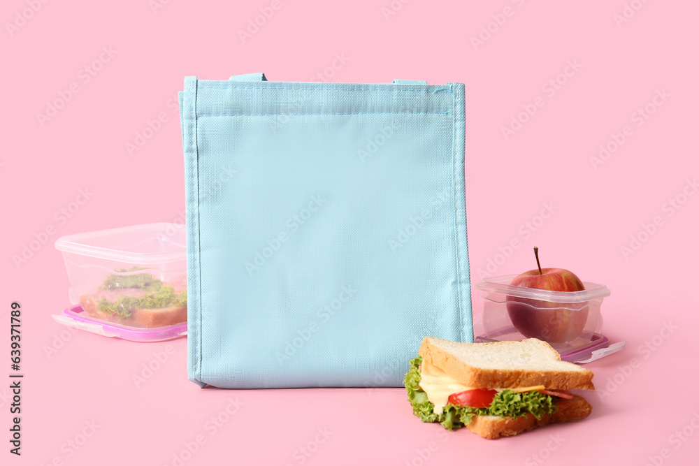 Bag, lunchboxes with delicious food and sandwich on pink wooden table near wall