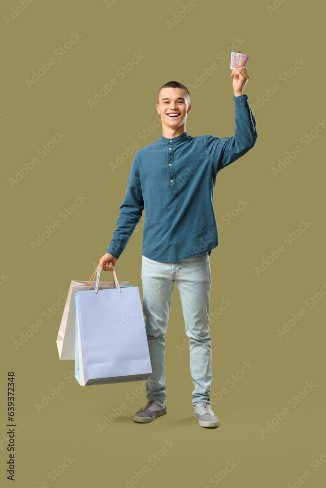 Young man with gift cards and shopping bags on green background