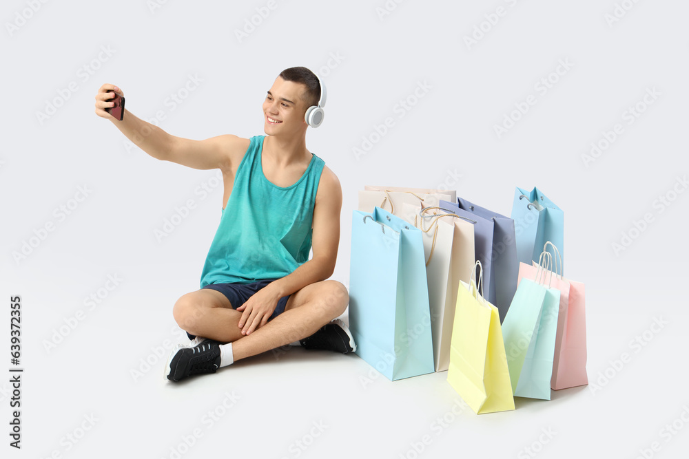 Sporty young man in headphones with shopping bags taking selfie on white background