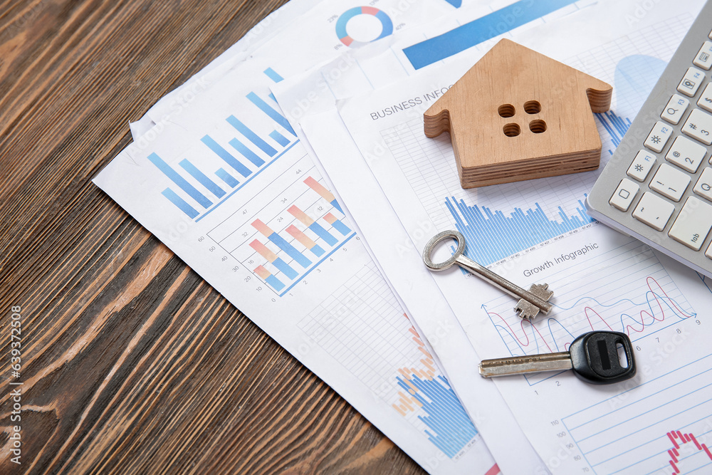 House figure with keys, diagrams and keyboard on brown wooden background. Concept of buying real est