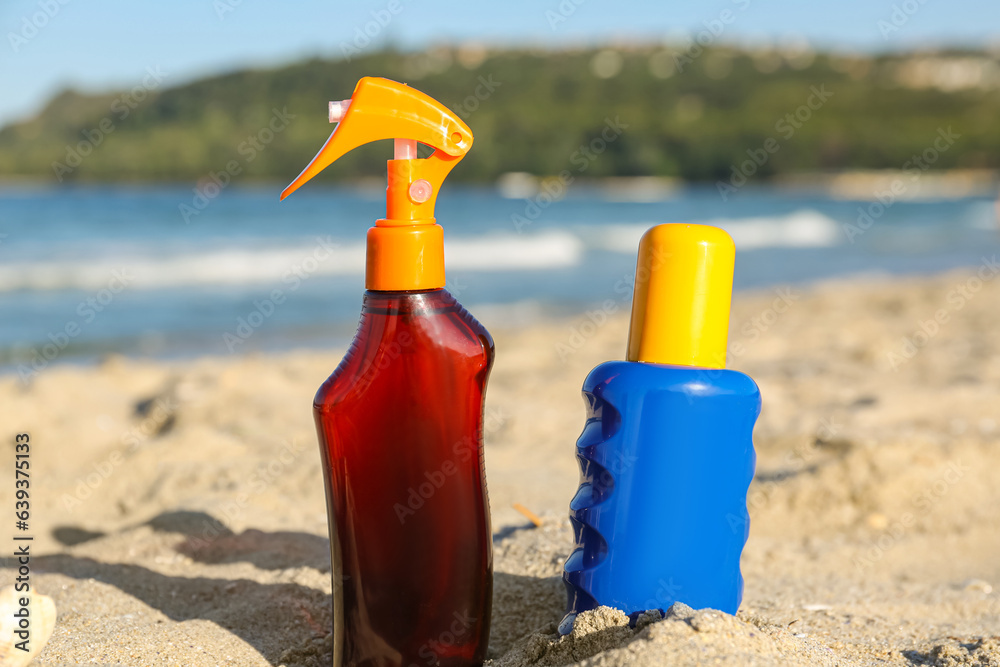 Bottles of sunscreen cream on sand near ocean at beach