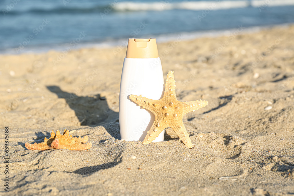 Bottle of sunscreen cream with starfish on sand near ocean at beach