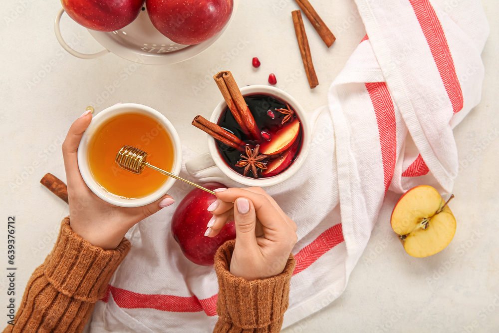 Female hands with bowl of honey and cup of hot mulled wine on white background