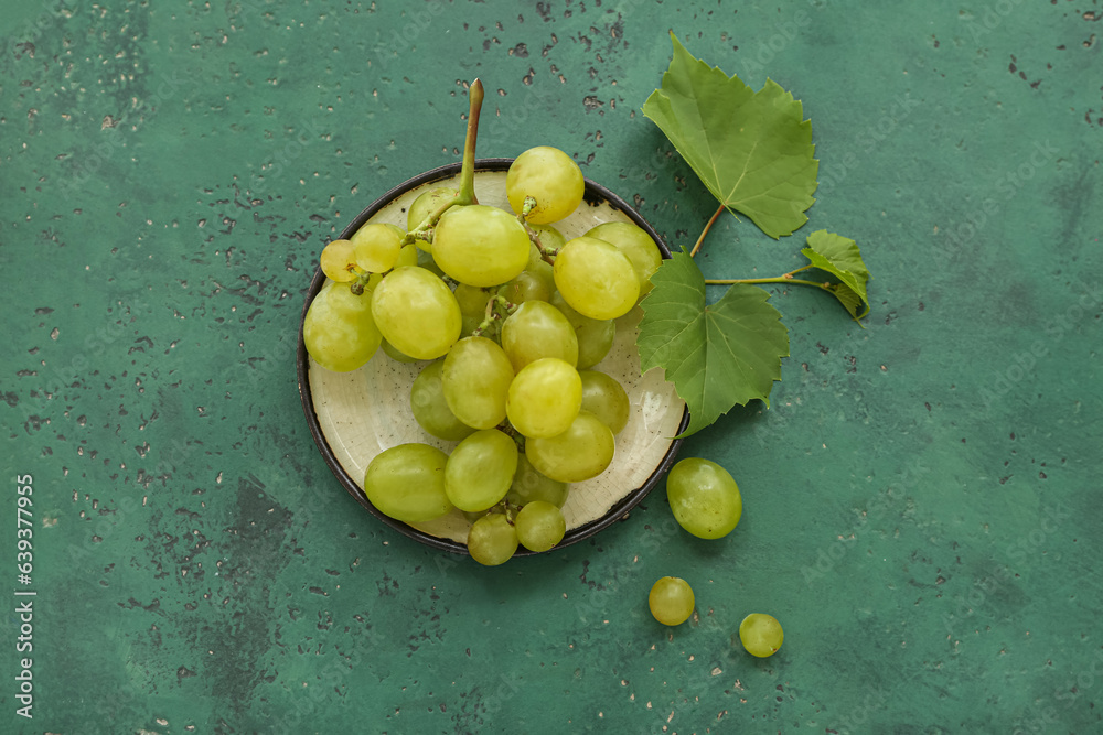 Plate with sweet green grapes and leaves on color background