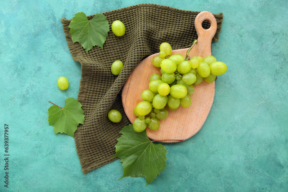 Wooden board with sweet green grapes and leaves on color background