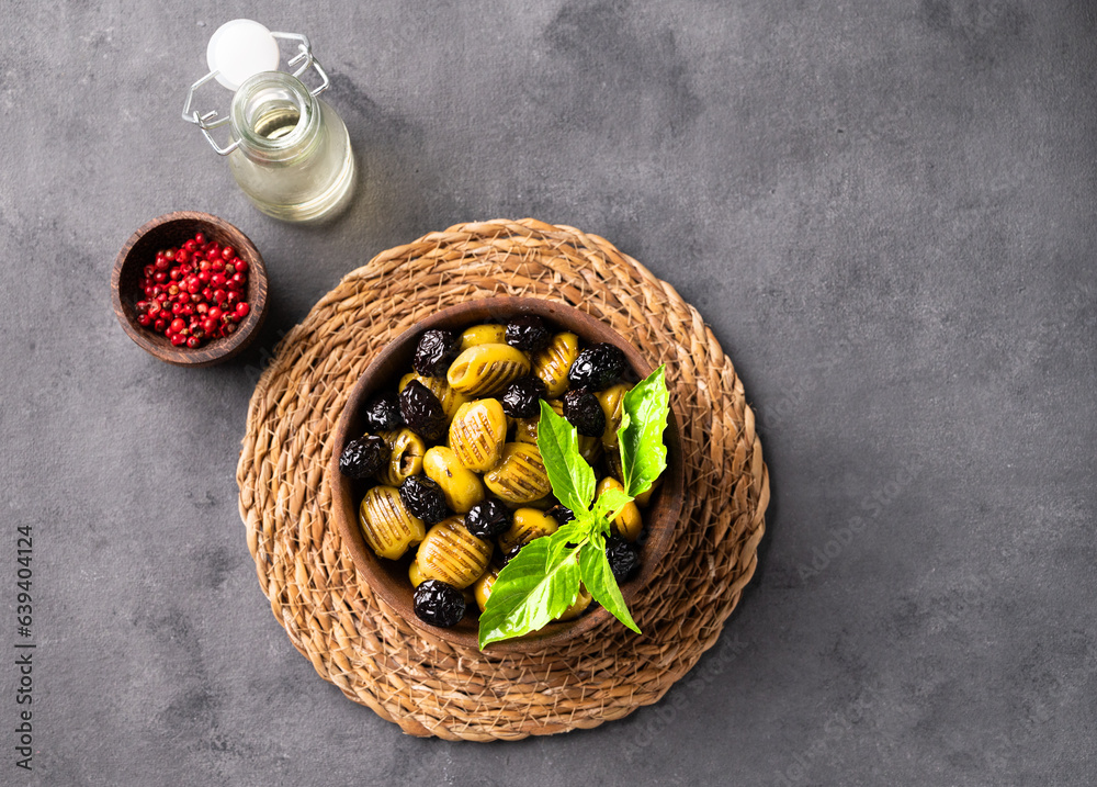 A set of green and black dried olives in bowl on a dark background with olive oil and red pepper. Th