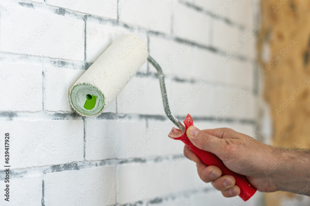 A worker paints a brick wall with white paint using a paint roller