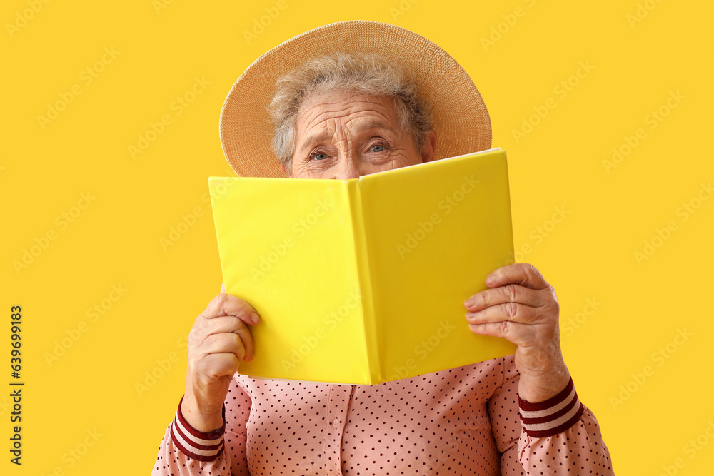 Senior woman reading book on yellow background, closeup