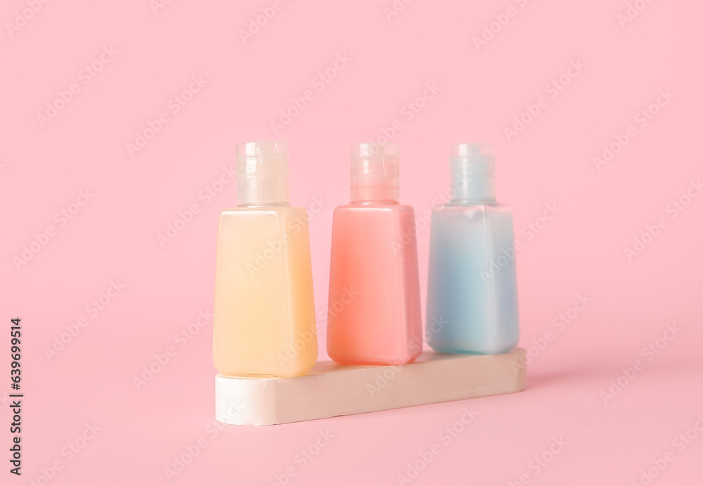 Plaster podium with bottles of different cosmetic products on pink background