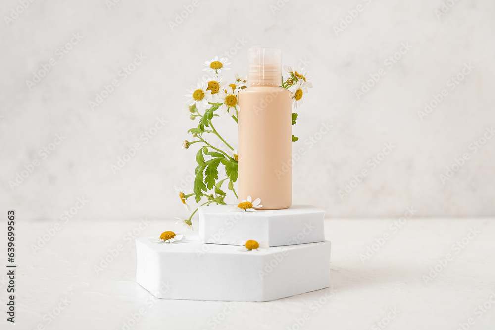 Composition with bottle of cosmetic product, plaster podiums and chamomile flowers on light backgrou