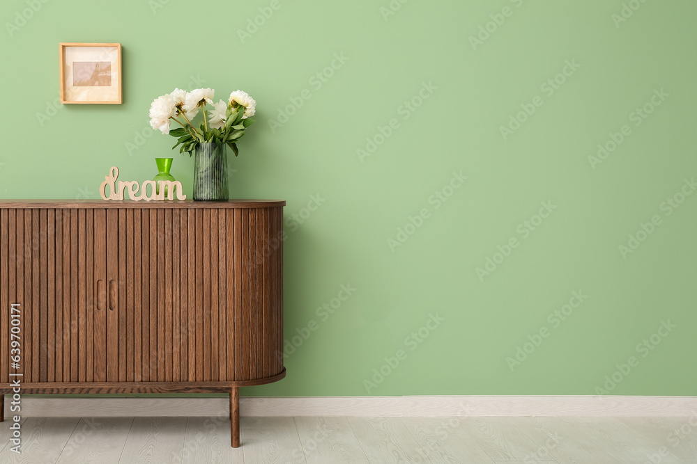 Vase of white peonies and decor in shape of word DREAM on dresser near green wall