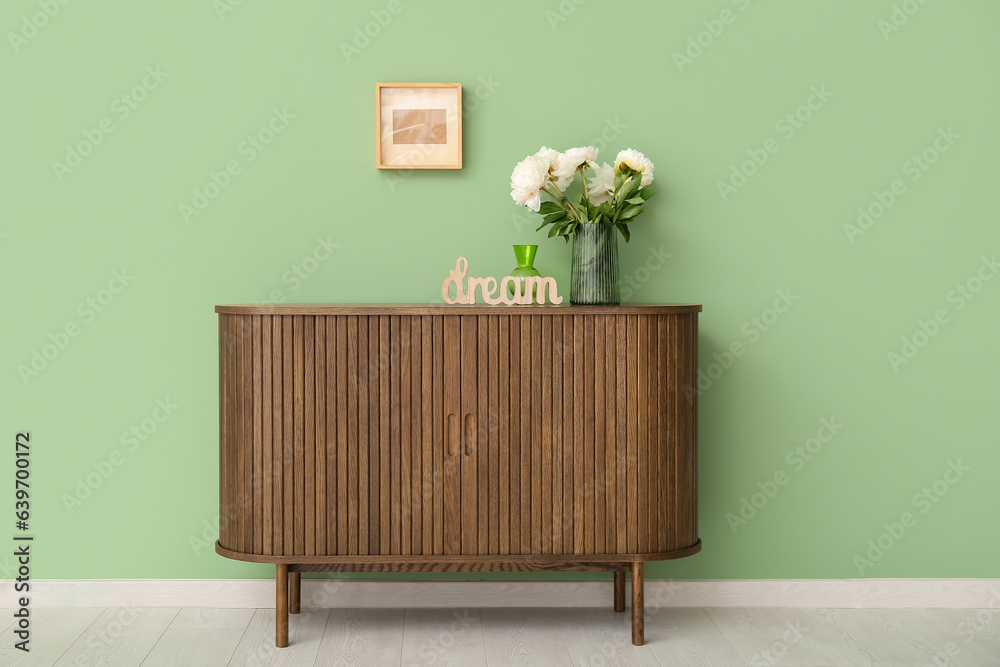 Vase of white peonies and decor in shape of word DREAM on dresser near green wall