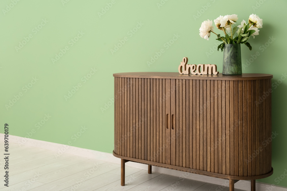 Vase of white peonies and decor in shape of word DREAM on dresser near green wall