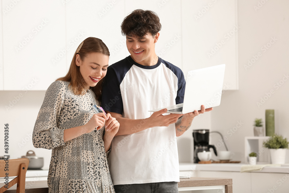 Young couple with laptop and gift cards shopping online in kitchen