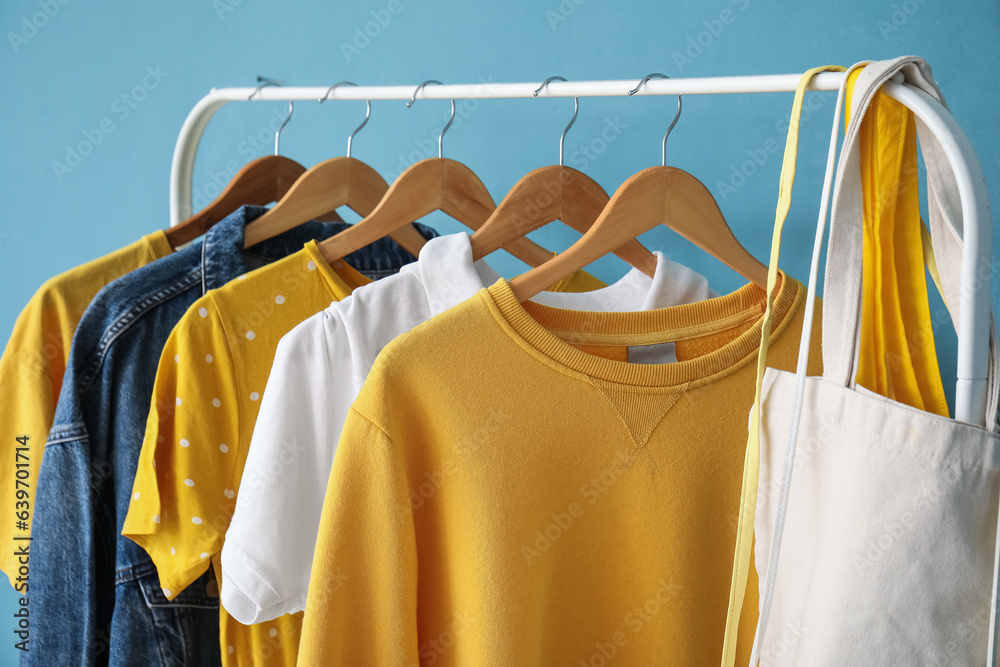 Rack with different clothes and bags on color background, closeup