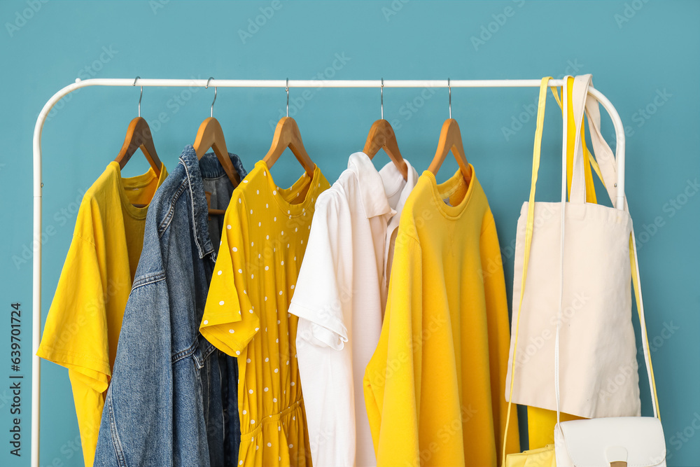 Rack with different clothes and bags on color background, closeup