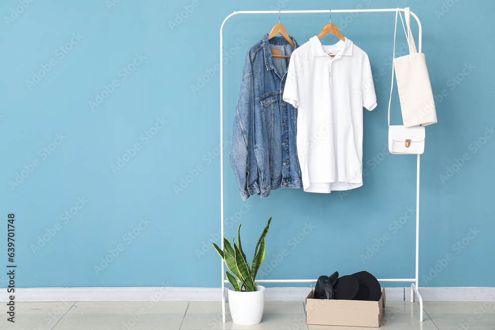 Rack with stylish clothes, accessories and houseplant near color wall