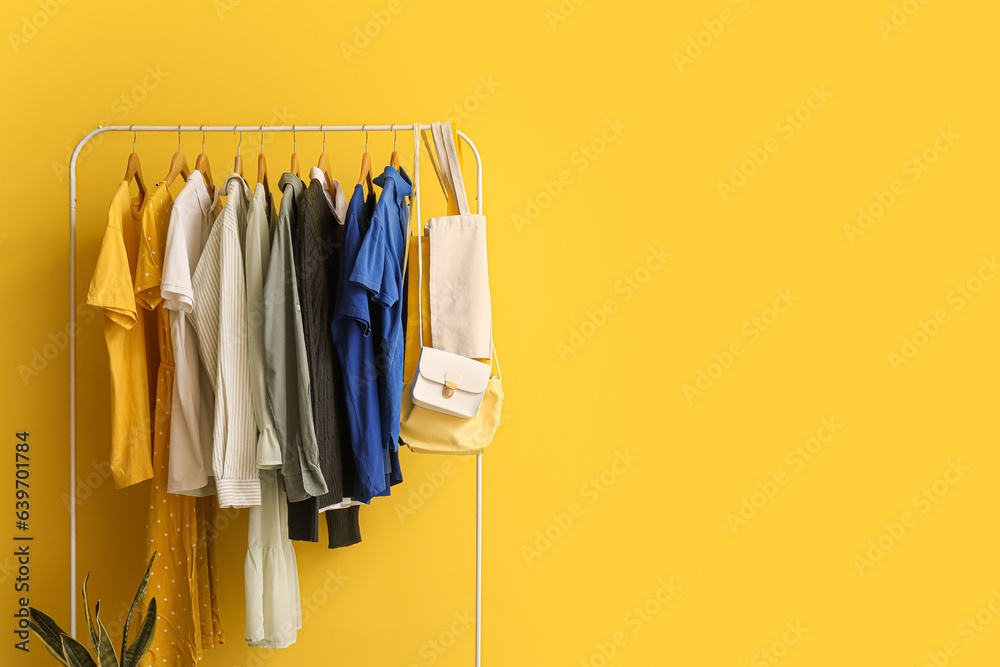 Rack with different clothes near yellow wall