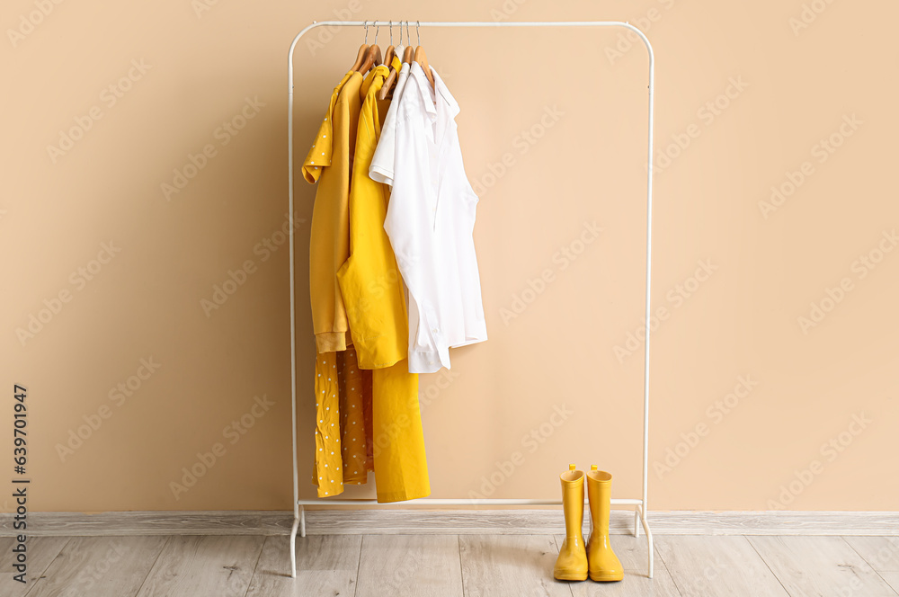 Rack with stylish clothes and rubber boots near color wall