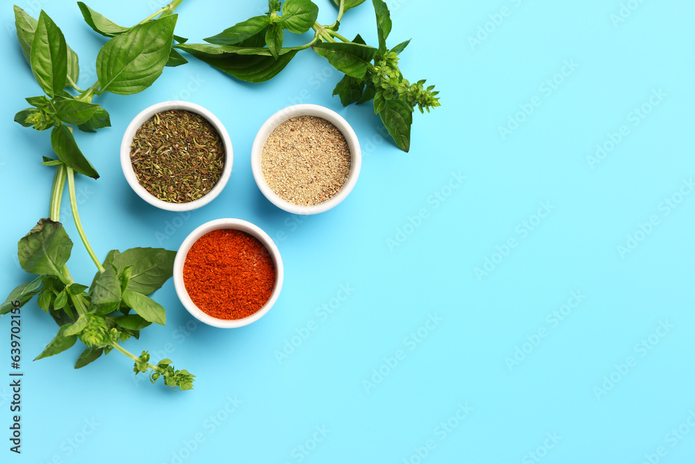 Bowls of aromatic spices and fresh basil on color background