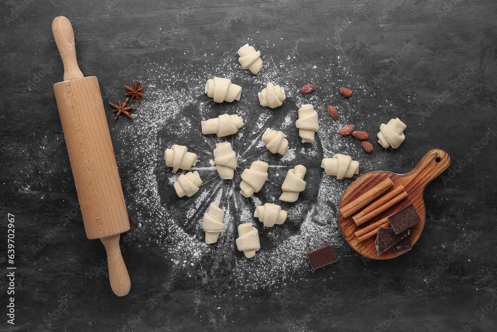 Composition with raw croissants, chocolate, spices and rolling pin on dark background