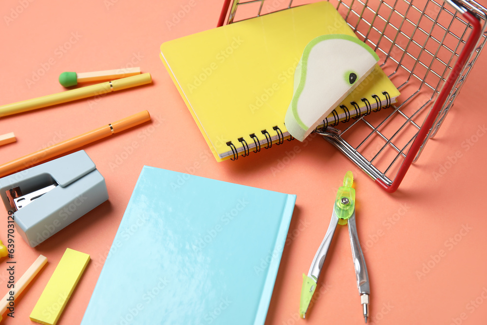 Overturned shopping basket with different stationery on color background, closeup