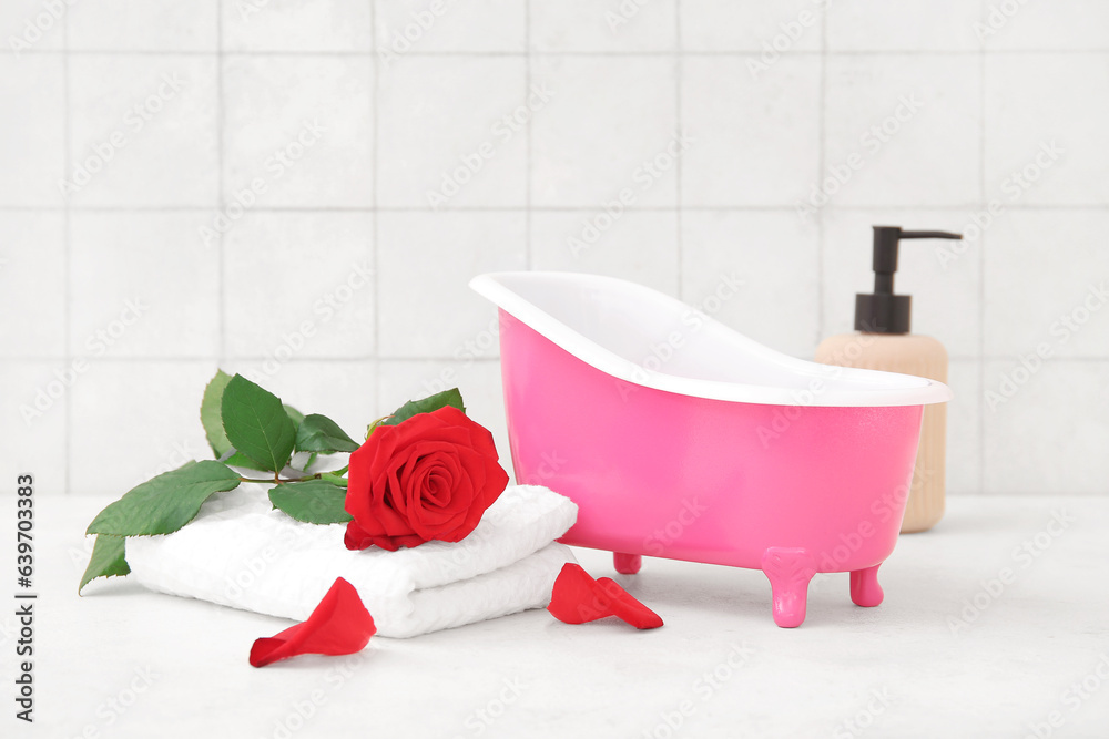 Small bathtub, rose flower and clean towel on light table