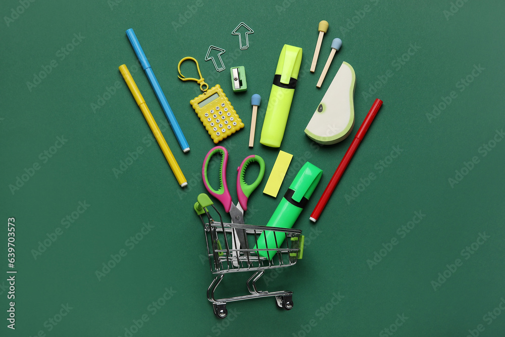 Shopping cart with different school stationery on green background