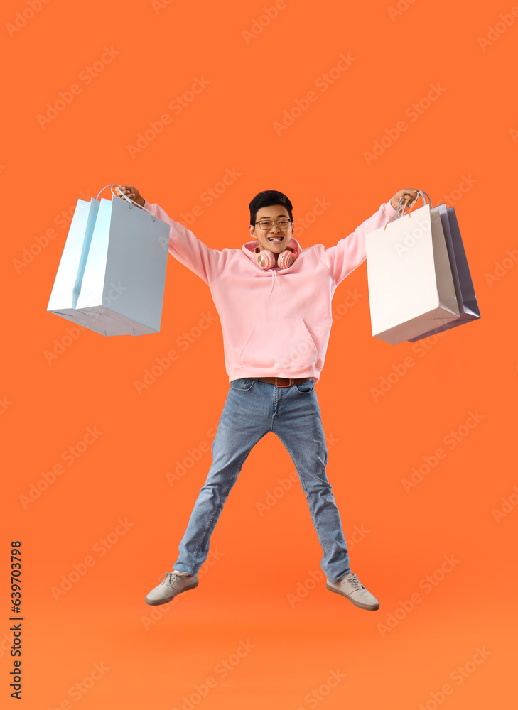 Young Asian man with shopping bags jumping on red background