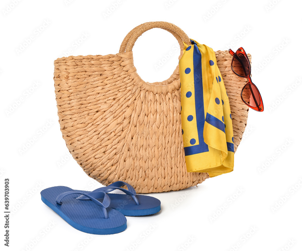 Wicker beach bag, sunglasses and flip-flops on white background