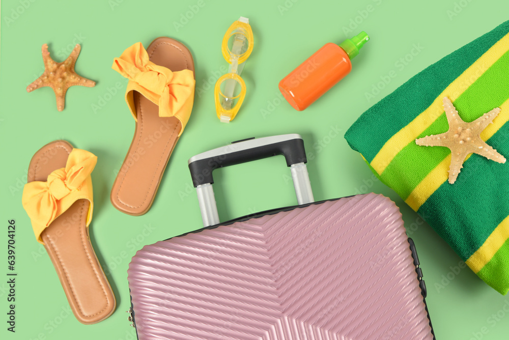 Composition with beach accessories and suitcase on green background, closeup