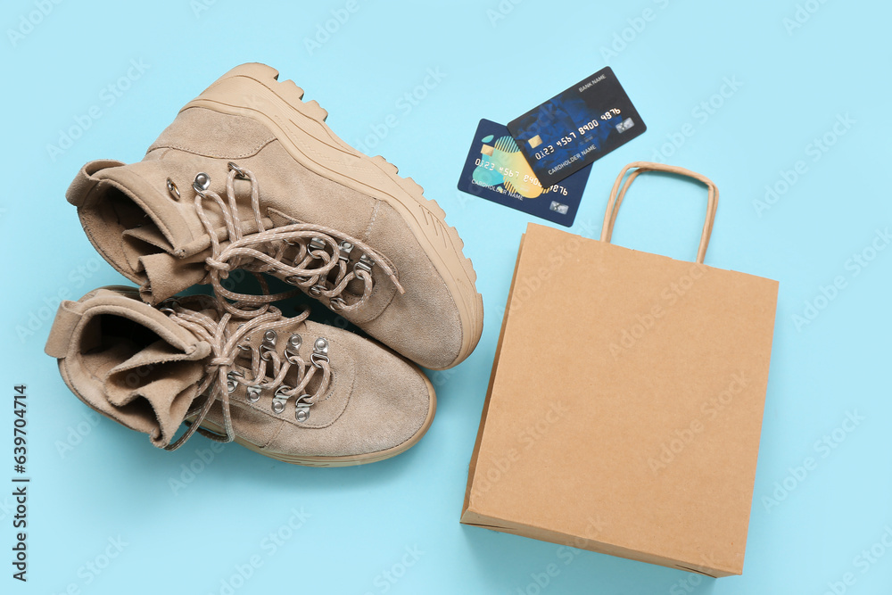 Pair of childs boots, shopping bag and credit cards on color background