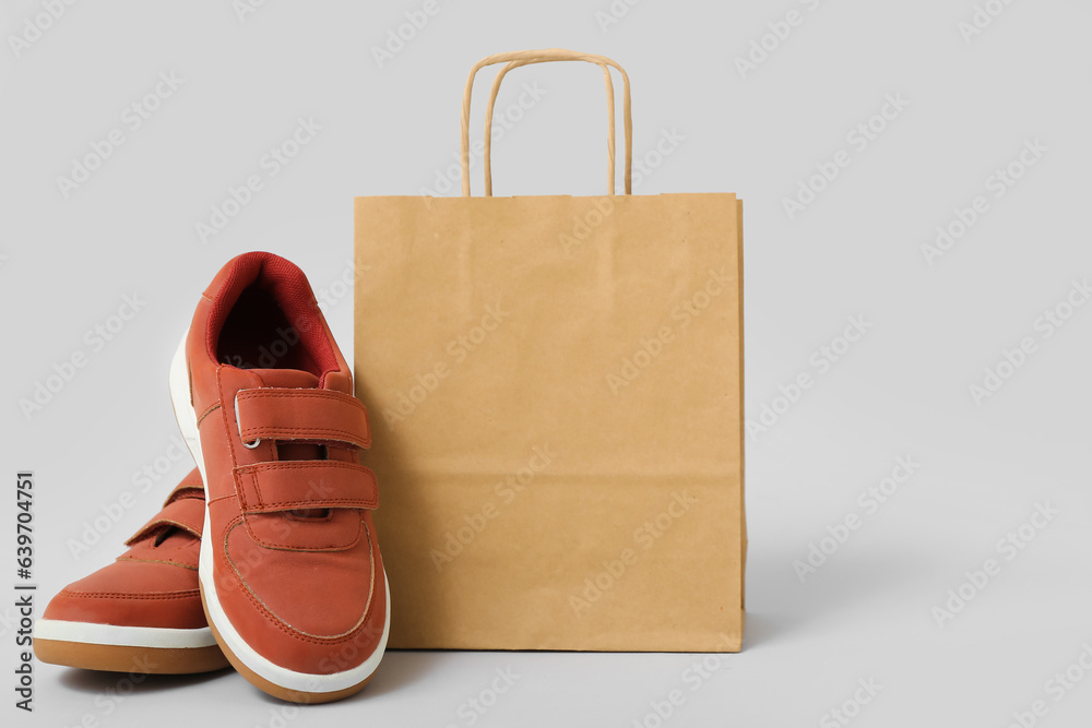 Paper shopping bag with stylish childs shoes on grey background