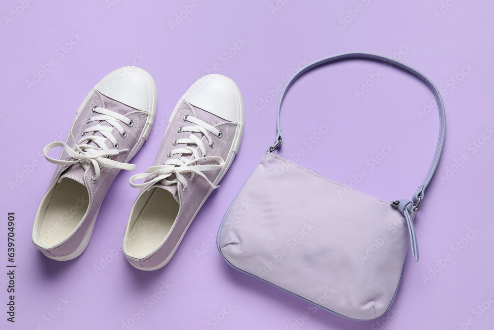 Stylish lilac sneakers and handbag on color background