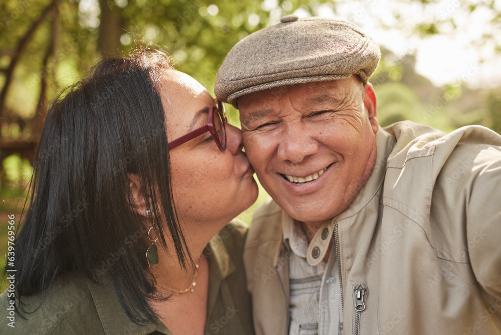 Selfie, kiss and senior couple in a park happy, bond and having fun in nature together. Portrait, lo