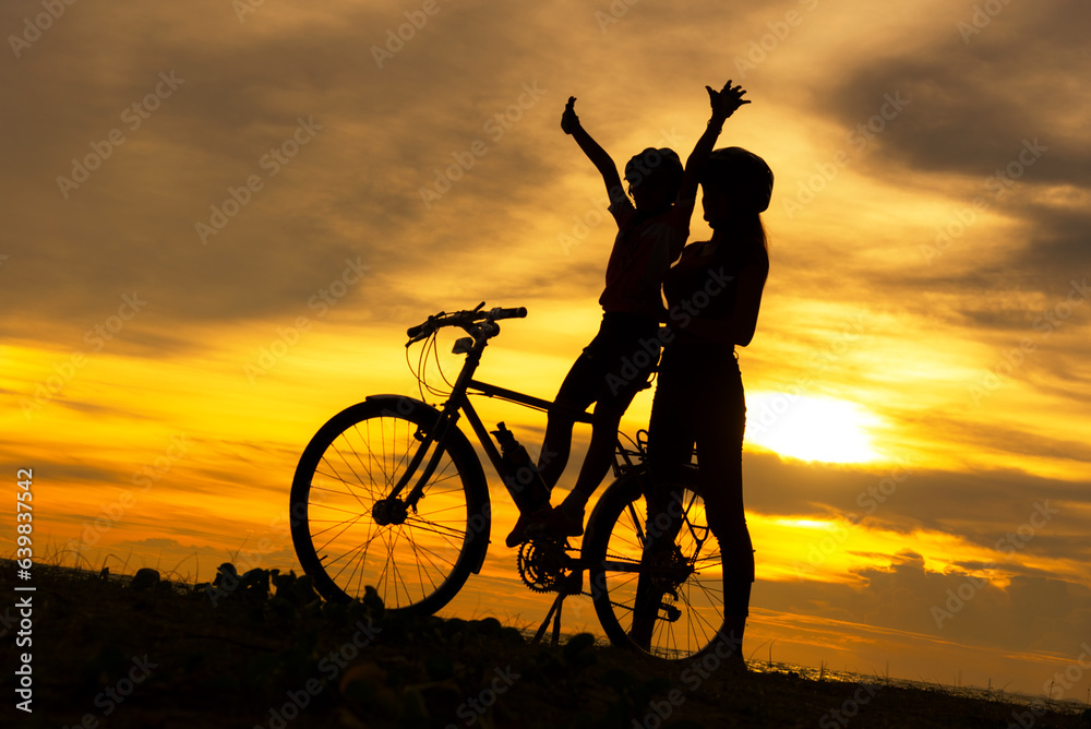 Silhouette biker lovely family sitting and talking at sunset over the ocean.  Mom and daughter bicyc