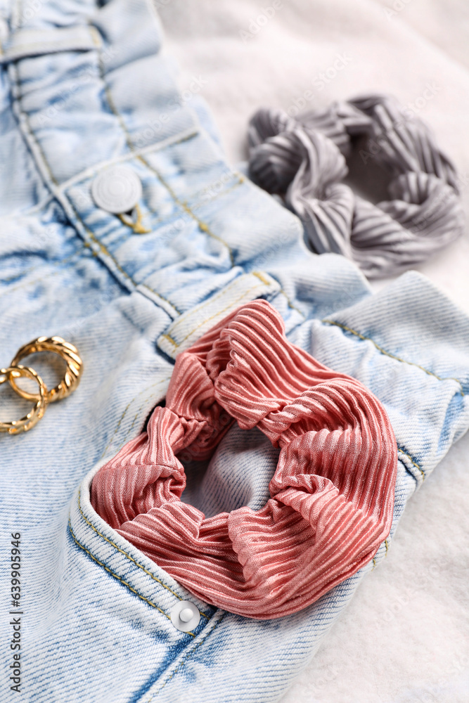 Silk scrunchies with jeans and rings on white fabric background, closeup