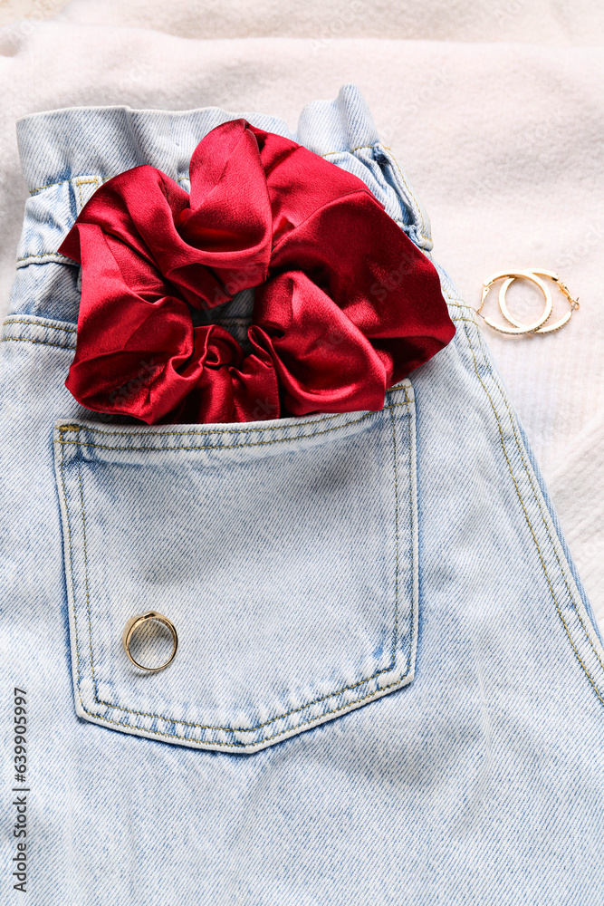 Silk scrunchy with jeans and jewelry on white fabric background, closeup