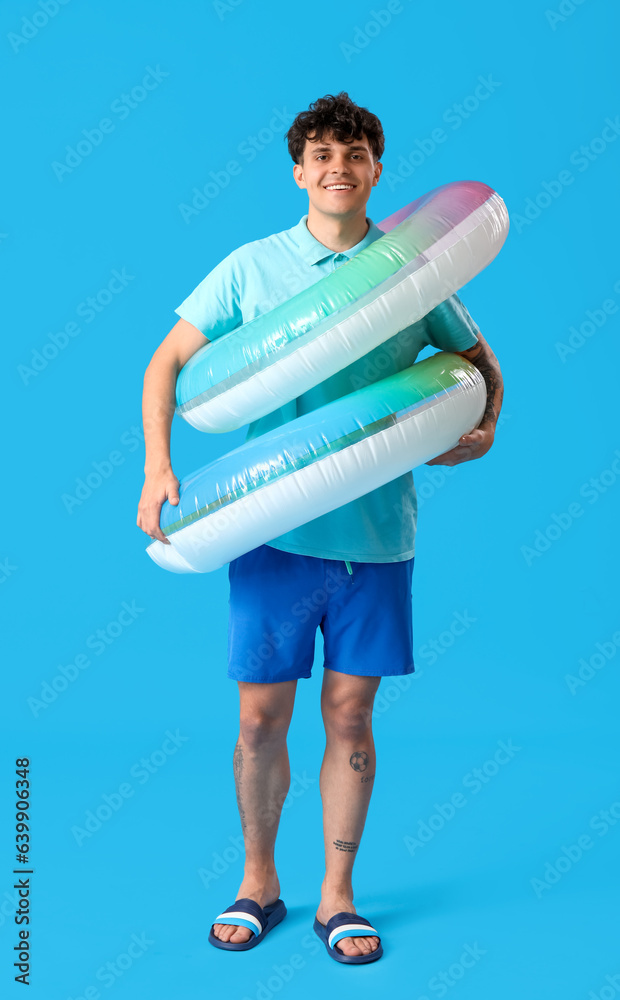 Young man with inflatable rings on blue background