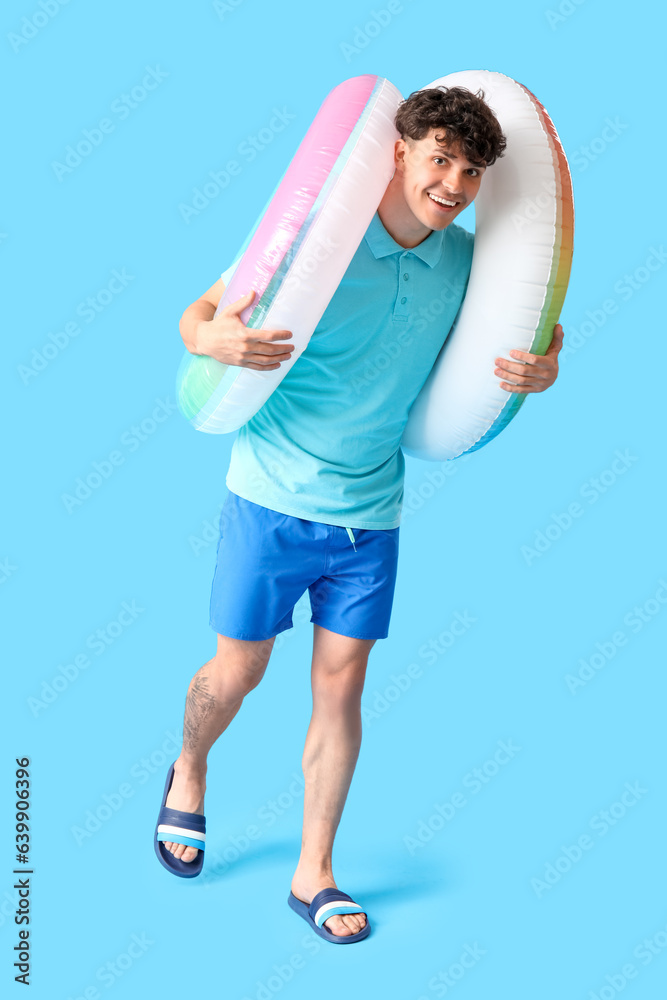 Young man with inflatable rings on blue background