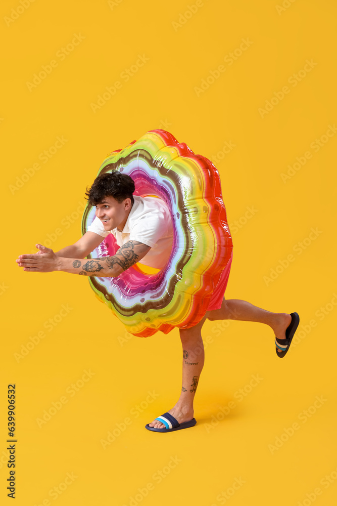 Young man with inflatable ring on yellow background