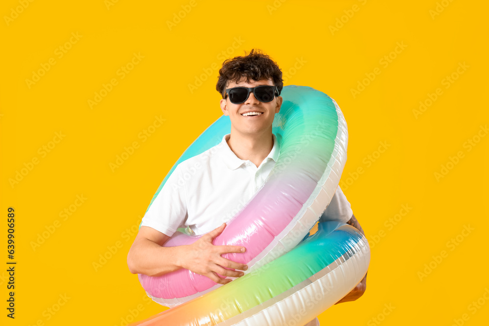 Young man with inflatable rings on yellow background